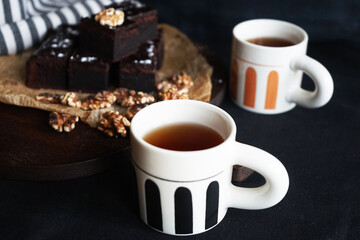 Chocolate cake with walnuts on a wooden board next to cups of tea on a dark background