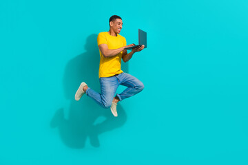 Full body profile portrait of active overjoyed young man jump run use netbook isolated on turquoise color background