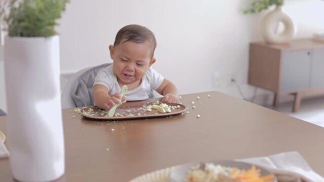 Latino baby smiling while eating breakfast and grabbing a pre-loaded spoon. Complementary feeding of a Latin baby. BLW