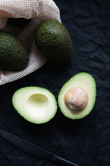 Cut ripe avocado next to other avocados on a dark background