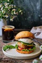 Homemade burger with cheese, lettuce, cucumber, tomato, chicken, poached egg. Wooden background, side view.