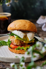 Homemade burger with cheese, lettuce, cucumber, tomato, chicken, poached egg. Wooden background, side view.