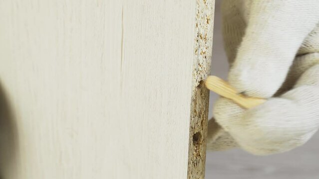 Furniture assembly, scrap. A worker hammers a wooden dowel into a hole of a smaller diameter and breaks a piece of furniture. Close-up.