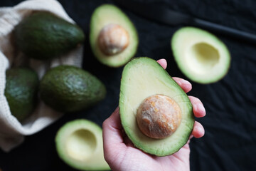Cut avocado in a woman's hand against the background of other avocados