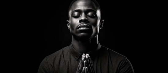One handsome young African American man is captured in a black and white portrait looking serene while meditating his hands in prayer position