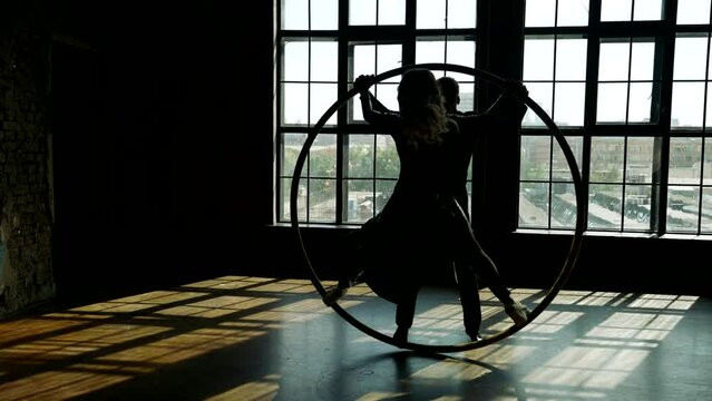 pair of man and woman dancing together and performing acrobatic trick with hoop, slow-motion