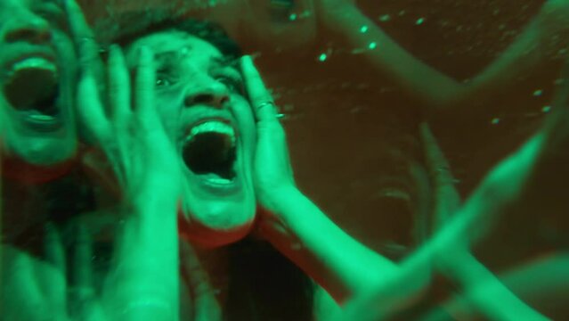 Mad girl looking at her reflection in the mirror, rubbing her face and screaming in fear, having a panic attack in a room with neon light. Kaleidoscope effect, mental disorder concept