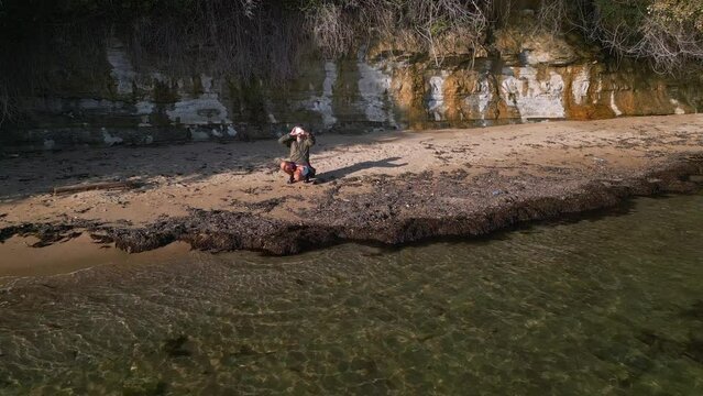 A man on the coast of the sea in a wilderness is signaling for help with a signal mirror