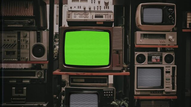 Vintage TV Green Screen Old Electronics Stack Static Noise Zoom In, VHS Texture. A pile of vintage electronics with a green screen television in the center, zoom in