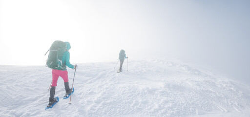 Fototapeta na wymiar climbers climb the mountain in the snow. Winter mountaineering. two girls in snowshoes walk through the snow. mountaineering equipment. hiking in the mountains in winter.
