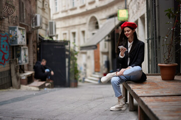 Woman standing near a wall in the city wearing a stylish jacket and red beret with red lips, travel and leisure, French style of dress, spring.