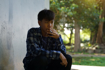 A teenage boy secretly comes to sit and smoke alone in a hidden corner of the school. which is the substance use behavior of teenagers who have life problems. soft and selective focus.  - obrazy, fototapety, plakaty