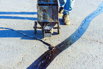 An asphalt patcher performs coated filling asphalt cracks sealing bitumen emulsion road surface...