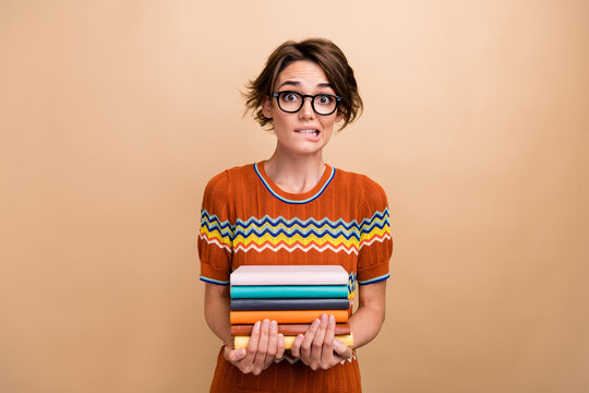 Portrait of nervous pretty girl arms hold pile stack book biting lips worry isolated on beige color background