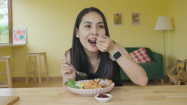 Asian woman enjoying and eating crispy pork chili paste rice during lunch in restaurant