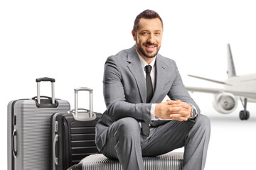 Bussinessman sitting on a suitcase in front of an aircraft