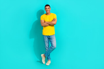 Naklejka premium Full body cadre of young man wear yellow trendy t-shirt denim jeans crossed arms confident posing model isolated on cyan color background