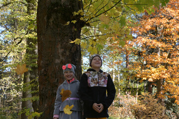 two smiling siblings brother and sister throw nicely colored autumn leaves into the air, close-up...