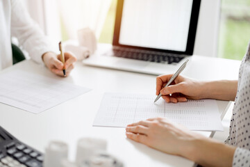 Two accountants using a laptop computer for counting taxes at white desk in office. Teamwork in business audit and finance