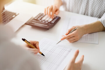 Accountant using a calculator and laptop computer for counting taxes with a client or a colleague at white desk in office. Teamwork in business audit and finance