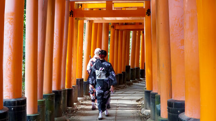 Obraz premium Woman dressed in kimono walking under torii gates at the Fushimi Inari Shrine.