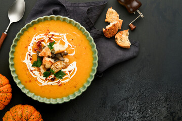 Pumpkin and carrot cream soup with herbs, seasonings and seeds in bowl on black wooden background in rustic style. Thanksgiving traditional autumn pumpkin cream soup. Top view.