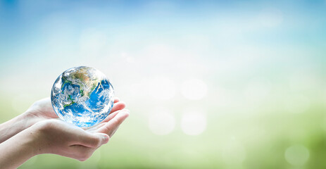 Human hand holding globe on blurred green and blue nature background. Elements of this image...