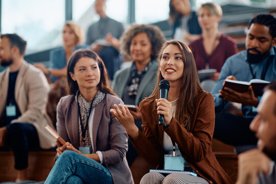 Young happy businesswoman talks on microphone while attending education event in conference hall.