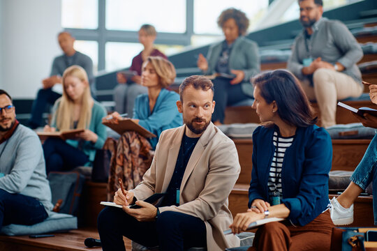 Business seminar attenders talk during lecture in conference hall.