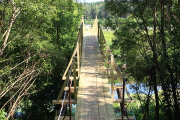 Obraz premium New wooden suspension bridge over the river for pedestrians in the countryside
