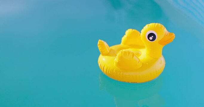 Inflatable yellow duck swims in swimming pool of clear blue water on sunny day