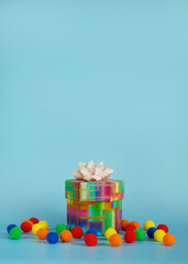 Gift box surrounded by colorful soft balls on a blue background. The concept of celebrating a birthday or other festive event. Copy space for your text