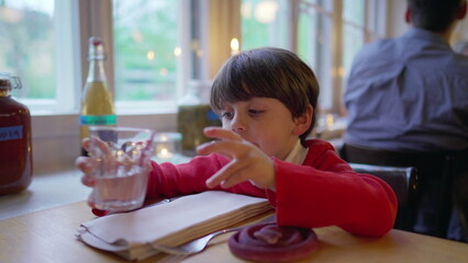 Childing drinking water at restaurant. Small boy hydrating himself wearing sweater and polo