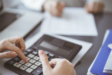 Woman accountant using a calculator and laptop computer while counting taxes for a client. Business...