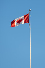 Canadian flag on pole in the wind with blue sky