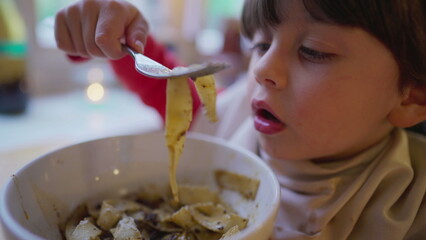 Little boy with napkin tucked into collar, delighting in spaghetti at restaurant. Child eating...