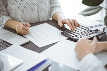 Woman accountant using a calculator and laptop computer while counting taxes with a client or a...