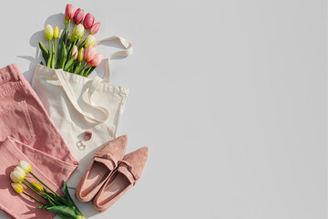 Fashion spring outfit. Pale pink jeans with bouquet of tulips flowers in bag,  and loafers. Women's stylish and elegant clothes with accessory and jewelry.  Flat lay, top view, overhead. - obrazy, fototapety, plakaty