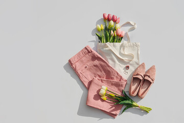 Fashion spring outfit. Pale pink jeans with bouquet of tulips flowers in bag,  and loafers. Women's stylish and elegant clothes with accessory and jewelry.  Flat lay, top view, overhead.