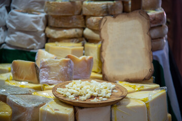 Detail shot of cheeses typical product of the Mediterranean diet with a wooden plate in the middle with samples in a street food market on a wooden table.