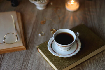 Vintage books, reading glasses, gold pen, hand model, gold jewelry, scented candles, flowers, chess pieces and cup of tea or coffee on the table. Dark academia concept. Selective focus.