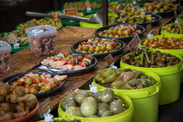 Detail shot of a street market stall full of different types of olives, gherkins, chillies, pickles...
