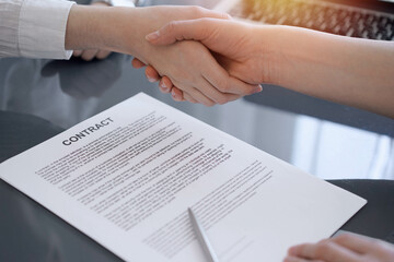 Business people shaking hands above contract papers just signed on the grey table, close up. Lawyers or entrepreneurs at meeting. Teamwork, partnership, success concept