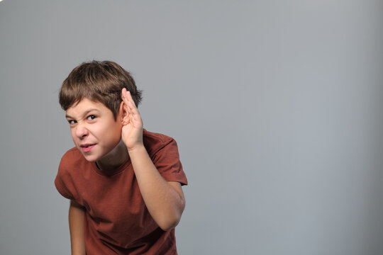 young boy with attentive expression holds his hand to his ear, signaling gesture of listening intently. listening skills in education, and challenges of maintaining focus in a digitally environment.
