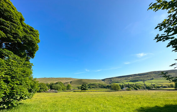 Landscape with wide open fields, trees, farm buildings, and distant hills near, Todmorden, UK