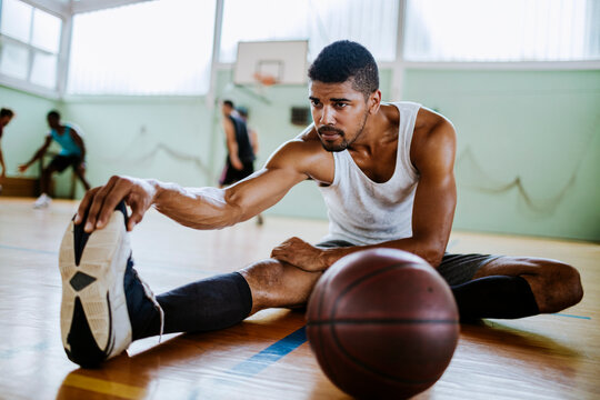 Young fit man stretching leg in basketball gym