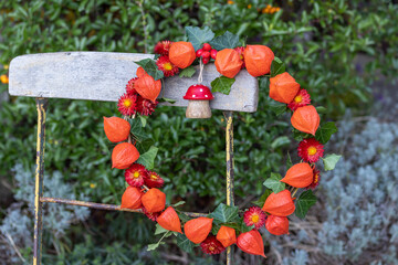 Kranz mit Physalis, Strohblumen und Efeublättern dekoriert mit Holzfliegenpilz hängend am...