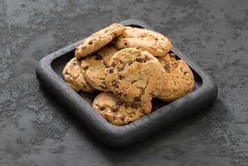 Round cookies with pieces of chocolate, on a wooden plate. Rustic style. Top view. Dark gray background	