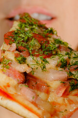 A woman puts a slice of pizza in her mouth. Soft selective focus.