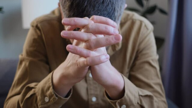 Close up of anxious sad young man sitting alone on sofa at home, worrying about difficult life situation, health problems or relationship troubles, lost in negative thoughts. Feeling insecure concept
